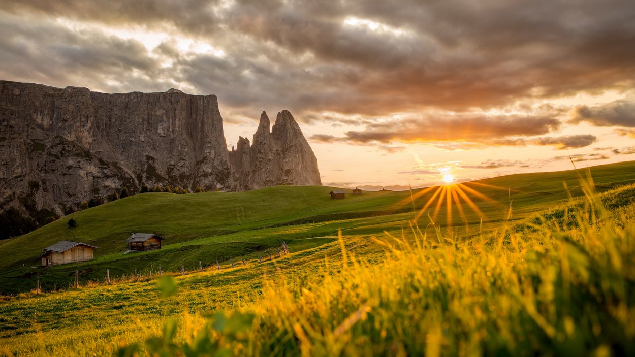 Schlern – unverwechselbares Bergmassiv Sonnenuntergang über grünen Hügeln und Felsen mit Holzhütten in den Alpen
