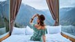 Boutiquehotels in Südtirol Frau mit Hut sitzt auf Bett vor Panoramafenstern mit Bergblick