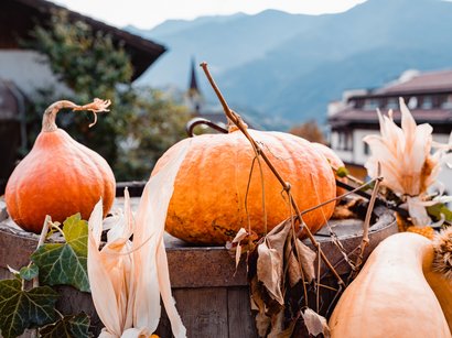 Törggelen in Südtirol: Topangebote mit Übernachtung Herbstliche Kürbisse und getrocknete Pflanzen auf einem Holzbottich vor Bergkulisse