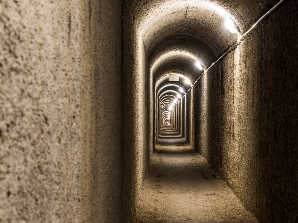 Gampen Bunker am Deutschnonsberg Beleuchteter Tunnel mit gewölbter Decke und sandigem Boden