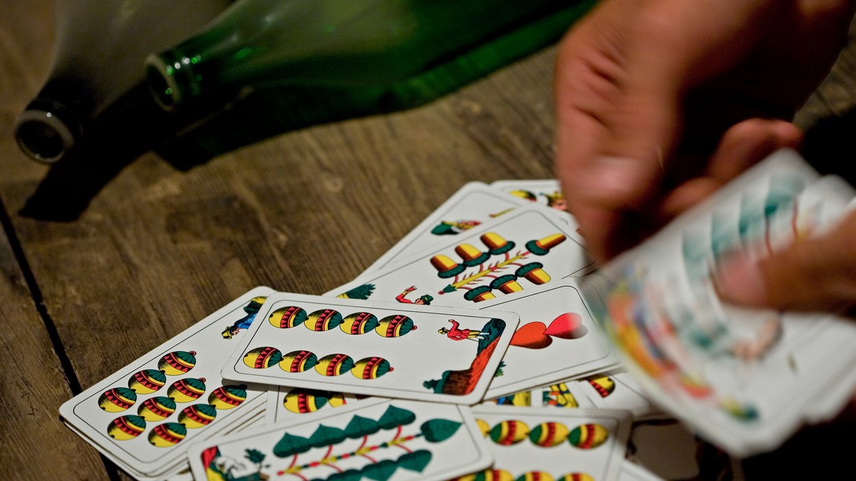 Watten – das beliebteste Kartenspiel Südtirols Hand mischt italienische Spielkarten auf Holztisch neben Flaschen
