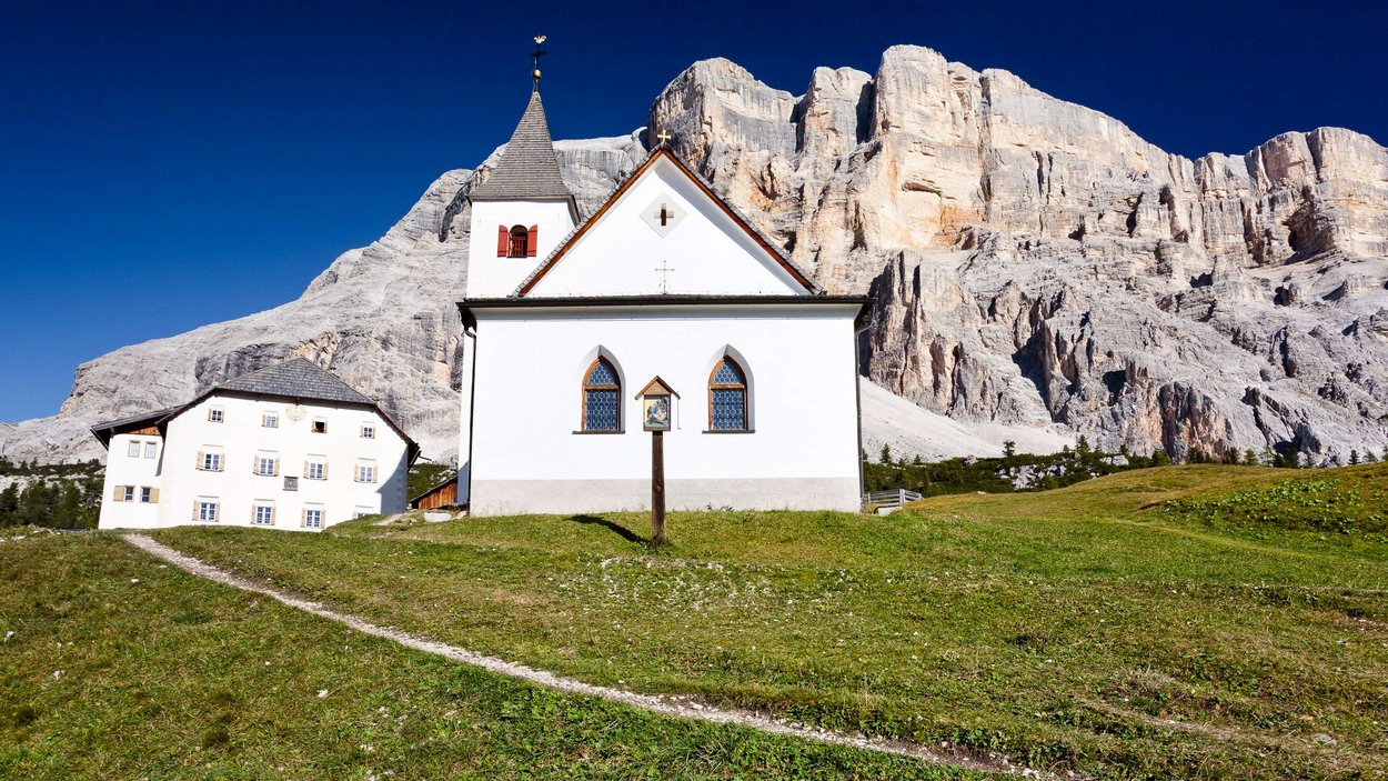 Il Sasso di Santa Croce Cappella bianca davanti a parete rocciosa sotto un cielo blu nelle Alpi