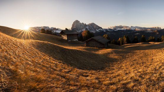Idyllischer Urlaub in den Hotels in St. Christina Sonnenaufgang über Hügeln und Holzhütten vor schneebedeckten Bergen