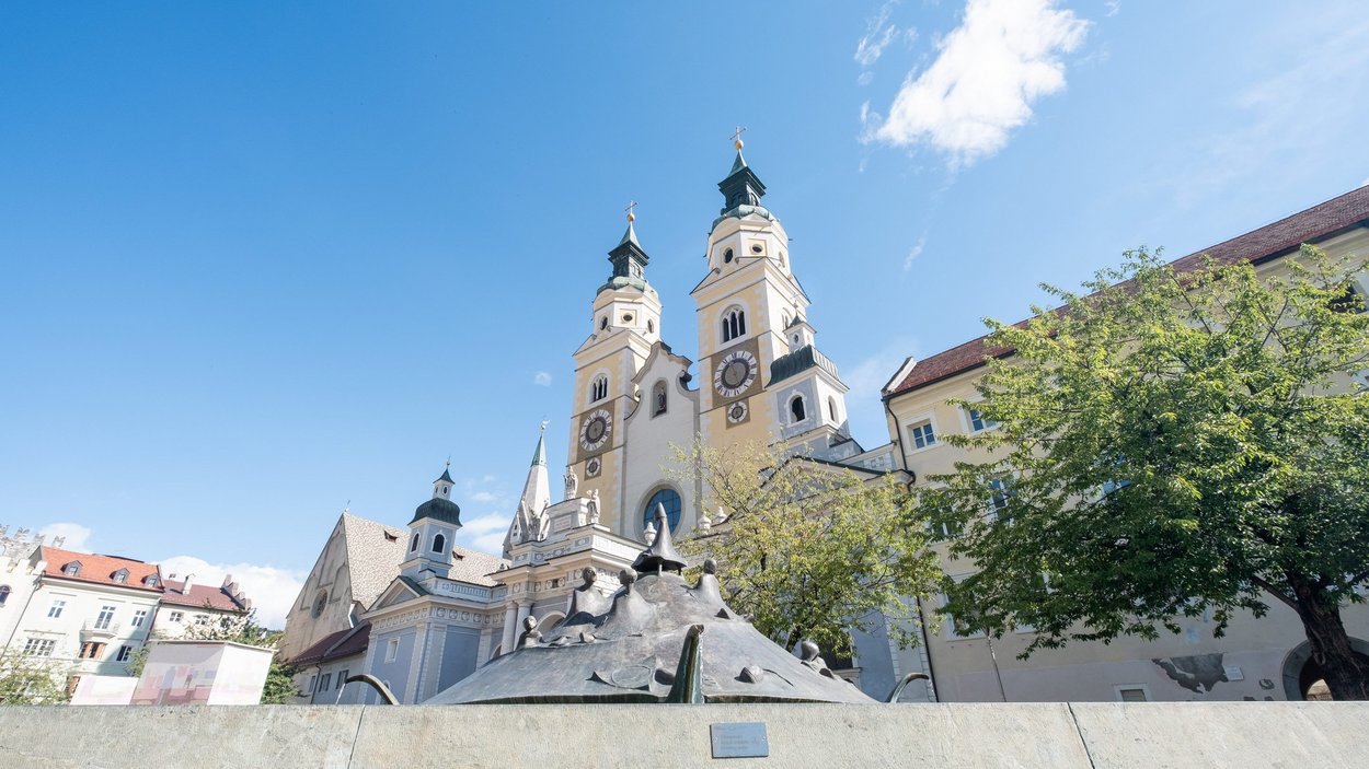 Hotels in Brixen, Südtirol, der ältesten Stadt Tirols Kirchturm mit zwei Uhren in einer historischen Stadt unter blauem Himmel