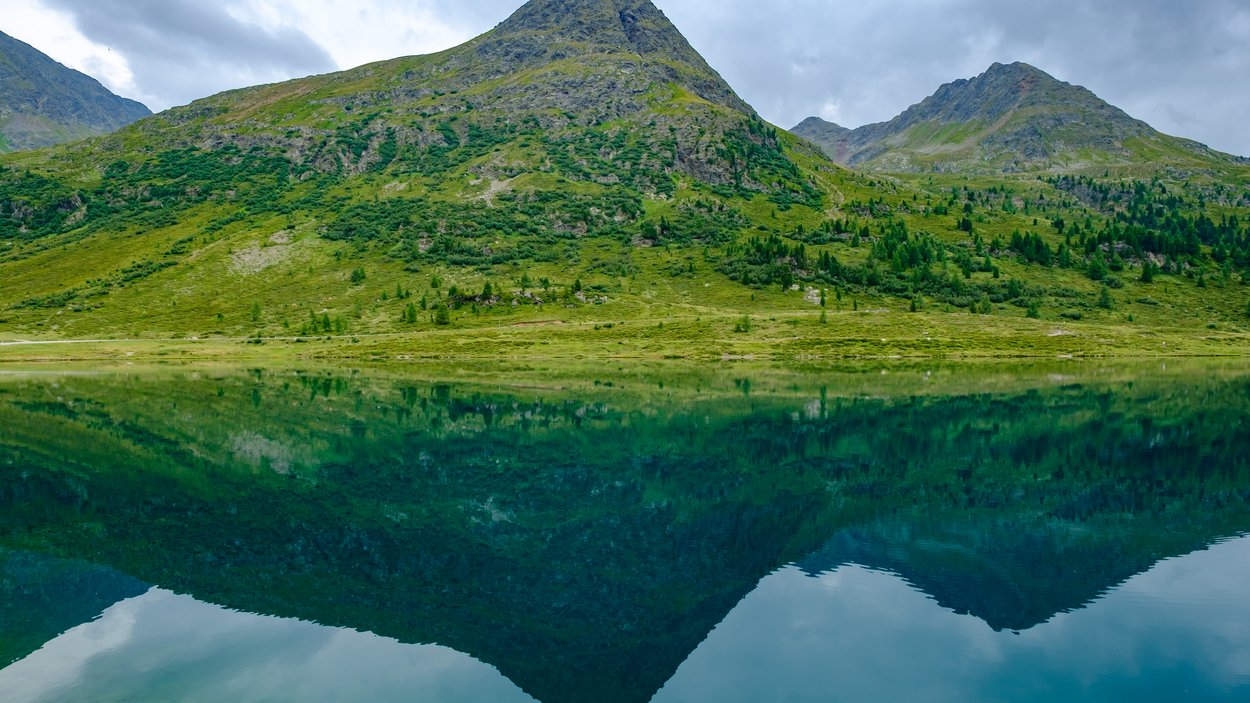 Staller Sattel: beliebtes Ausflugsziel in Südtirol Berg spiegelt sich im klaren See unter bewölktem Himmel