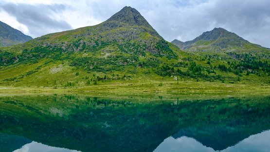 Staller Sattel: beliebtes Ausflugsziel in Südtirol Berg spiegelt sich im klaren See unter bewölktem Himmel