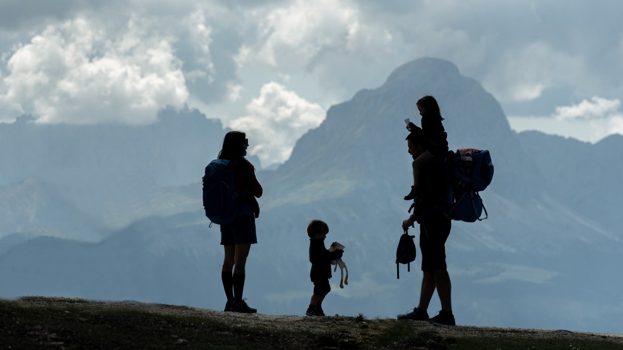 Escursione al Vorbichl Sagome di una famiglia in escursione con montagne e nuvole sullo sfondo