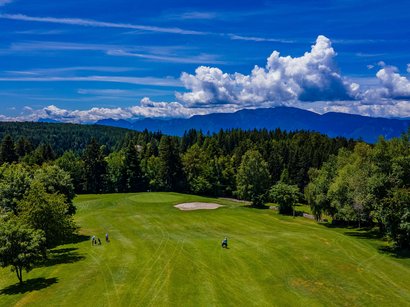 Hotel in Obereggen gesucht: Gastfreundschaft gefunden Golfplatz mit Spielern vor bewaldeten Hügeln und blauem Himmel mit Wolken