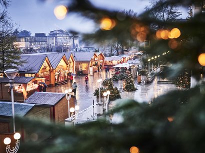 Ihre Hotels in Meran in Südtirol: Hotels im Meraner Land Weihnachtsmarkt mit beleuchteten Holzhütten und festlicher Dekoration bei Abenddämmerung