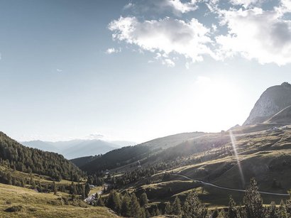 Golfen in Südtirol Sonnenstrahlen über einem bewaldeten und bergigen Tal bei klarem Himmel