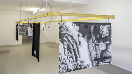 ar/ge Kunst – Bozner Kunstverein Schwarze und weiße Fototücher hängen an gelben Gestellen in einer weißen Galerie