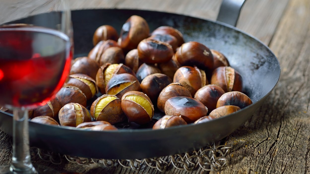 Törggelen in Alto Adige: le migliori offerte con pernottamento Castagne arrostite in una padella con un bicchiere di vino rosso in primo piano