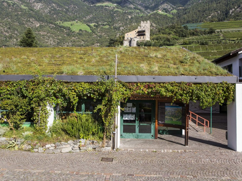 Naturparkhaus Texelgruppe Gebäude mit begrüntem Dach und Naturparkhaus-Schild, bewaldete Berge im Hintergrund