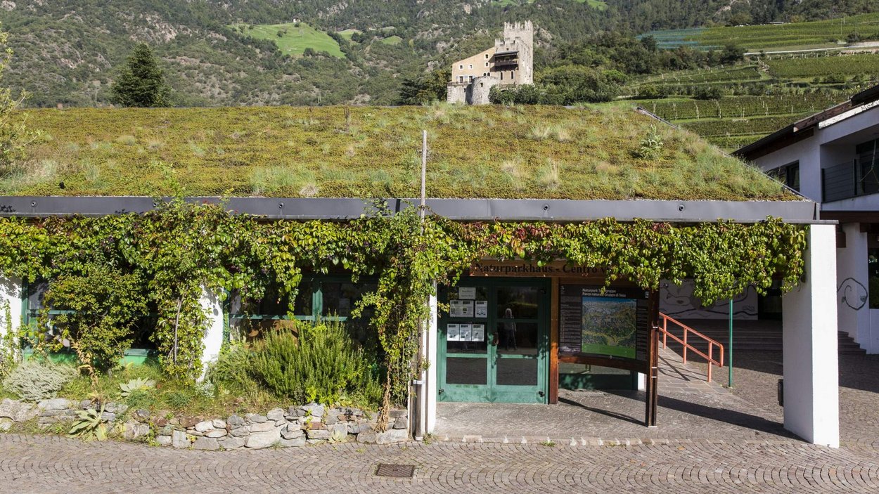 Naturparkhaus Texelgruppe Gebäude mit begrüntem Dach und Naturparkhaus-Schild, bewaldete Berge im Hintergrund