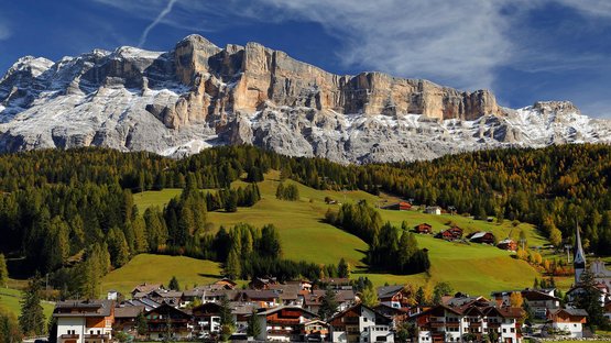 Die Sellagruppe in den Dolomiten Dorf am Fuße schneebedeckter Berge mit grünen Wiesen und Wäldern