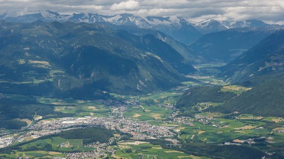 Hotel a Riscone presso Brunico Vista di una valle con paesi, campi e montagne sotto un cielo nuvoloso
