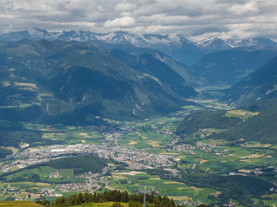 Hotel a Riscone presso Brunico Vista di una valle con paesi, campi e montagne sotto un cielo nuvoloso