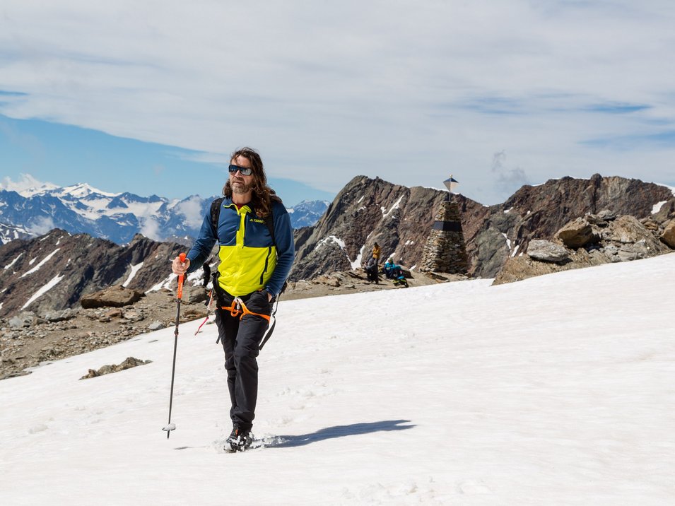 archeoParc Schnalstal Mann wandert mit Trekkingstock auf schneebedecktem Berg im Alpinen Gebirge
