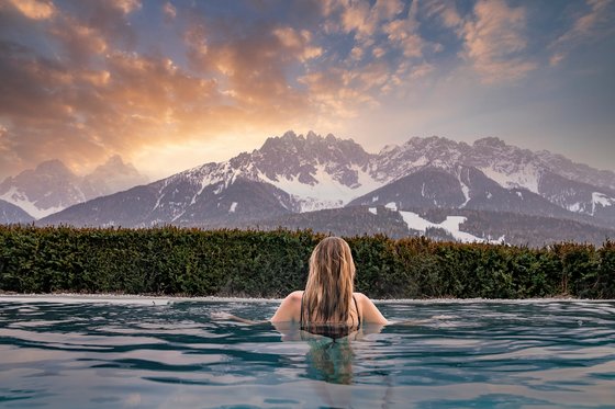 Die besten Wellnesshotels in Südtirol: Zeit für erholsame Stunden Frau schwimmt im Pool mit Blick auf schneebedeckte Berge bei Sonnenuntergang