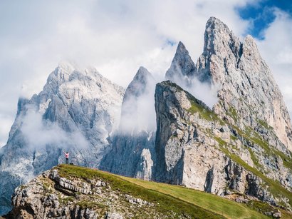 Klettersteig: Arzalpenturm Wanderer auf grünem Hügel vor beeindruckenden Dolomitenfelsen und Nebel