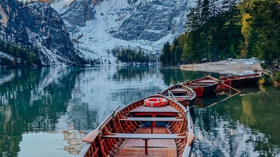 Vacanze in Alto Adige da non perdere Barche a remi su lago di montagna calmo con montagne innevate e foresta sullo sfondo