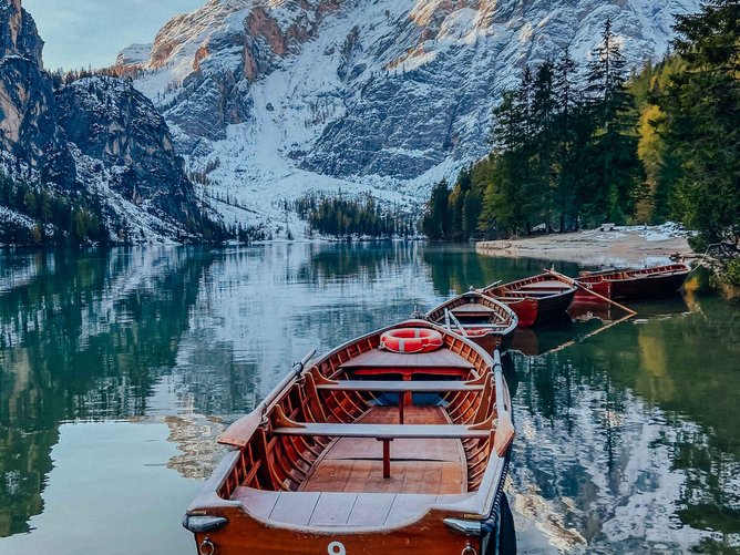 Erlebnisreicher Urlaub in Südtirol Ruderboote auf ruhigem Bergsee mit schneebedeckten Bergen und Wald im Hintergrund