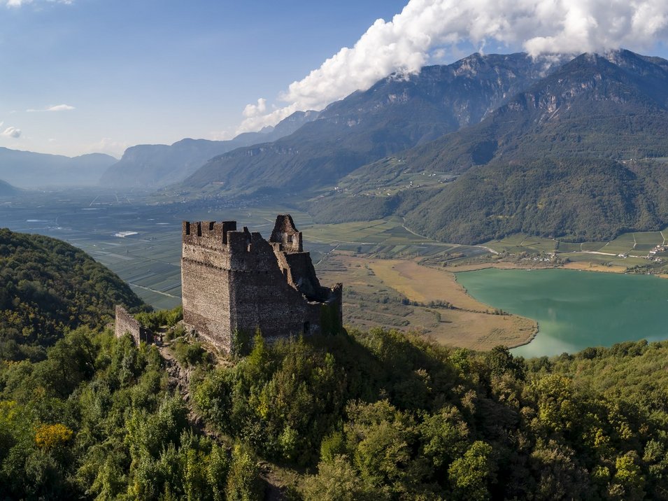 Die Leuchtenburg bei Kaltern Burg über bewaldetem Hügel mit See und Bergen im Hintergrund