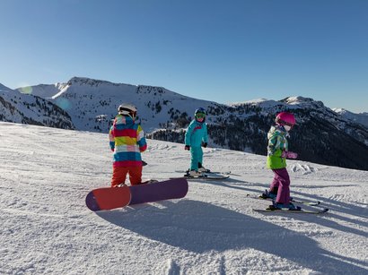 La Sellaronda, per girare attorno al massiccio del Sella Tre bambini con abbigliamento invernale su montagna innevata con sci e snowboard