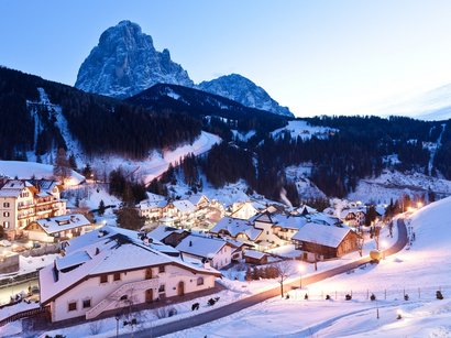 In den Hotels in Corvara den Urlaub genießen Schneebedecktes Dorf bei Sonnenuntergang vor hohen Bergen