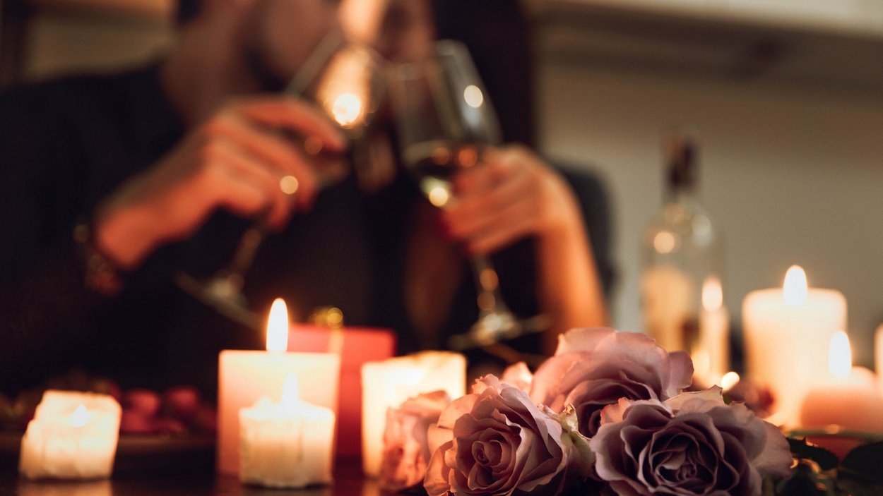 Romantische Hotels Südtirol – Urlaubsträume in den Bergen Romantisches Abendessen mit Rosen, Kerzenlicht und einem Paar mit Weingläsern