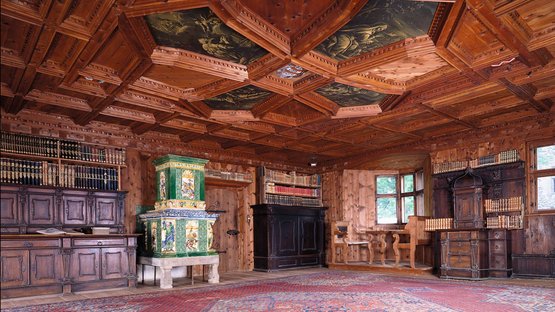 Castel Tures: tra storia e vista da sogno Stanza storica con pannelli in legno, soffitto dipinto, stufa verde e scaffali con libri