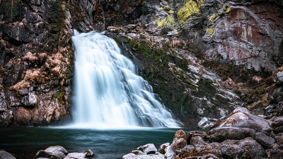 Reinbach-Wasserfälle bei Sand in Taufers Wasserfall fließt über Felsen in einen ruhigen Bergsee
