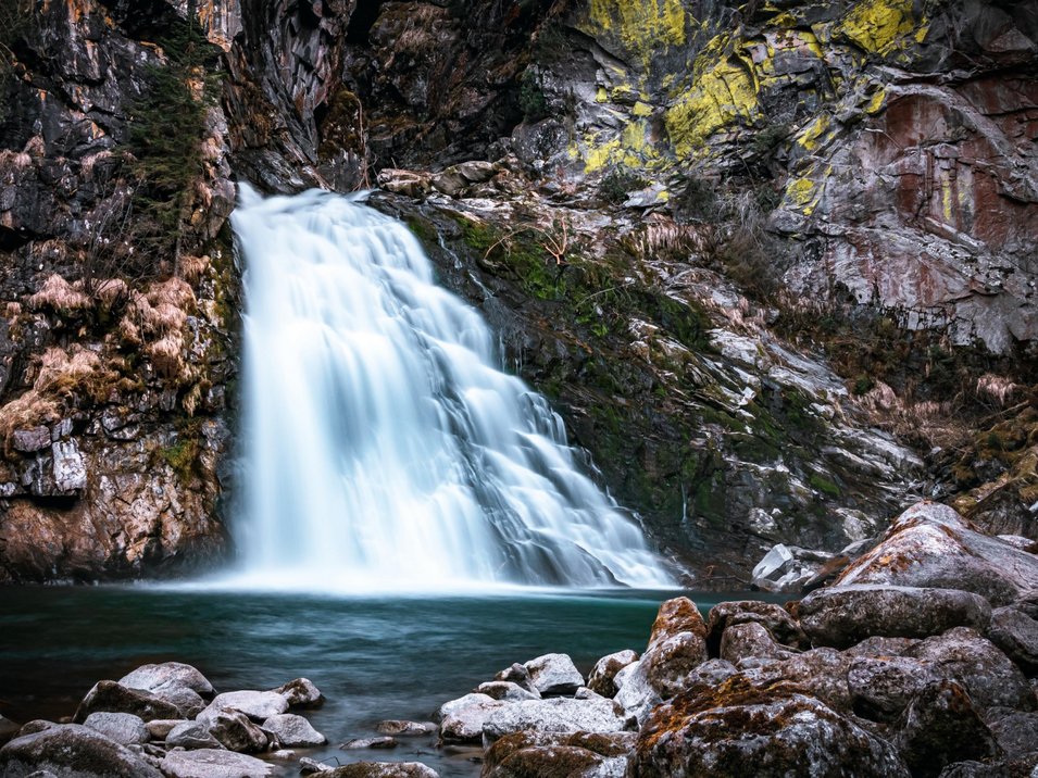 Reinbach-Wasserfälle bei Sand in Taufers Wasserfall fließt über Felsen in einen ruhigen Bergsee