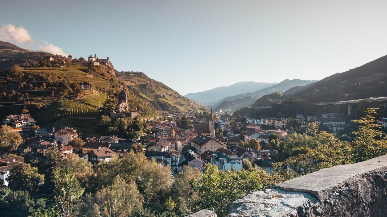 Hotels in Klausen: Ferien in Südtirol Blick auf eine Stadt mit Bergen und Burgen im Hintergrund bei klarem Himmel