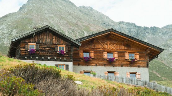 Echt Südtirol: Almen Traditionelle Holzhütten auf einem grünen Berghang mit Bergkulisse