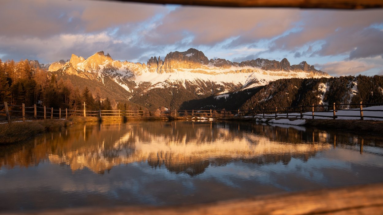 Hotels in Deutschnofen: Urlaub in den Dolomiten Schneebedeckte Dolomiten spiegeln sich im Wasser eines kleinen Teichs bei Sonnenuntergang