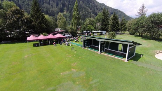 Der Golfclub Sterzing Golfübungsplatz mit Menschen vor Berghügeln und Bäumen