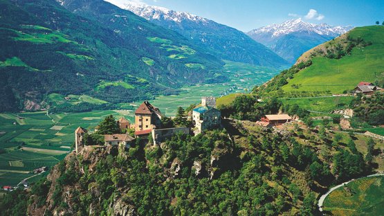 Schloss Juval bei Naturns Burg auf bewaldetem Hügel mit Tal und schneebedeckten Bergen im Hintergrund