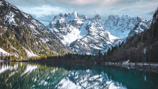 Lago di Landro: un caldo lago alpino sulle Dolomiti Montagne innevate riflesse in un lago alpino calmo sotto un cielo nuvoloso