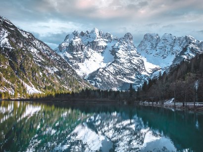 Der Pragser Wildsee im Hochpustertal in Südtirol Verschneite Berge spiegeln sich im klaren Bergsee unter bewölktem Himmel