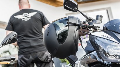 Rund um den Latemar Motorradhelm hängt am Lenker eines Motorrads, Mann im Hintergrund