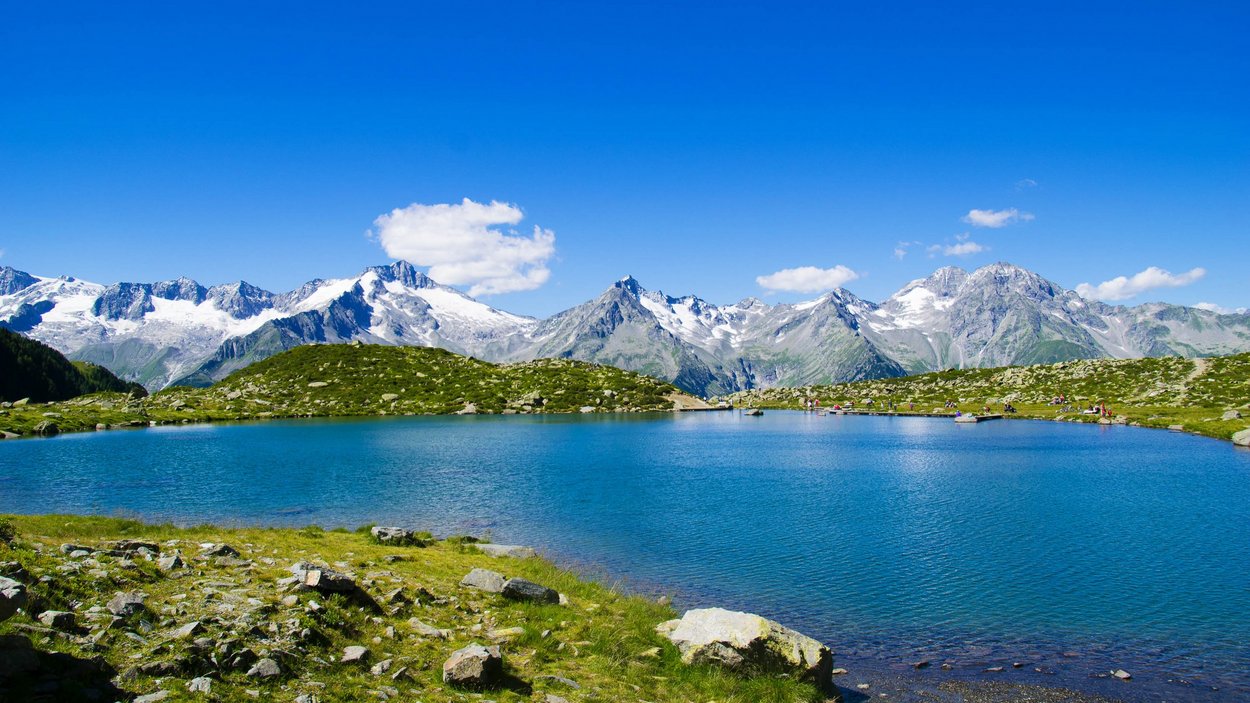 Hotel a Cadipietra in Alto Adige Lago di montagna con sponde verdi e cime innevate sotto un cielo azzurro