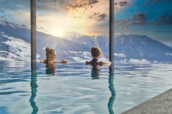 Ski-in/Ski-out in Südtirol Zwei Frauen entspannen im Infinity-Pool mit Aussicht auf schneebedeckte Berge im Sonnenuntergang