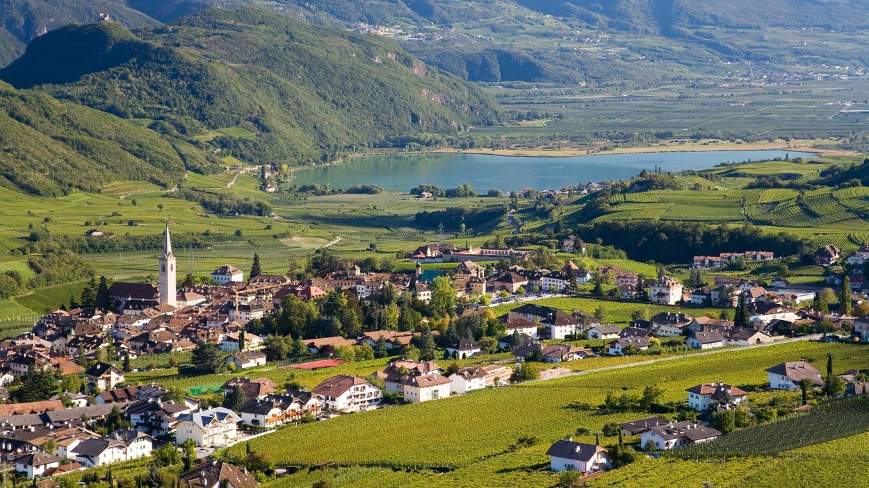 Strada del Vino dell’Alto Adige, un paradiso escursionistico Villaggio in una valle verde con vigne e lago sullo sfondo