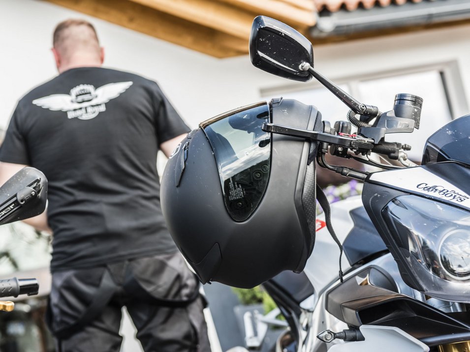 Attorno all’Adige, tour in moto in Alto Adige Casco appeso al manubrio di una moto, persona sullo sfondo