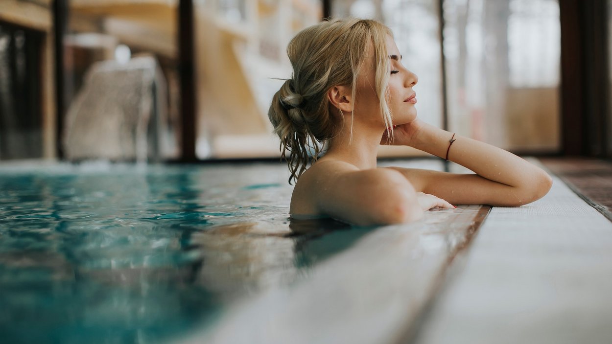 Day Spa nei migliori hotel benessere dell'Alto Adige Donna rilassata in piscina coperta appoggiata al bordo con gli occhi chiusi