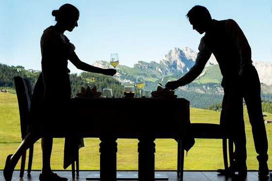 Unterkunft mit Infinity Pool in Südtirol Zwei Personen decken einen Tisch mit Wein vor Berglandschaft
