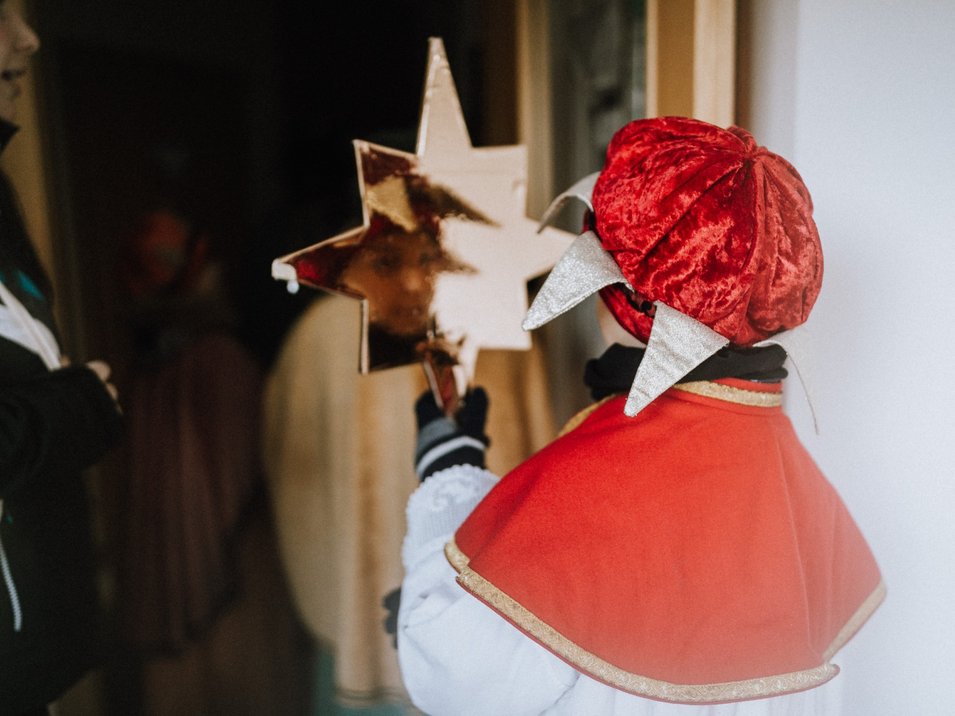 Mercatino di Natale di Brunico Bambino vestito con mantello rosso che tiene una stella dorata