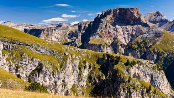 Hotels in Gröden in den Dolomiten! Berglandschaft mit grünem Gras und steilen Felsen unter blauem Himmel