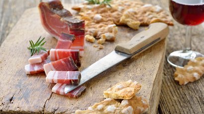 Alpe di Siusi Speck affettato, pane croccante e un bicchiere di vino rosso su tagliere di legno